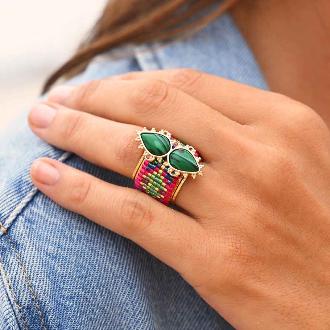 Hand wearing a colorful ring with green gemstones on denim fabric
