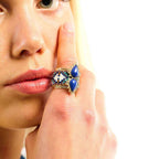 Close-up of a woman's hand wearing a decorative ring with blue stones on a white background