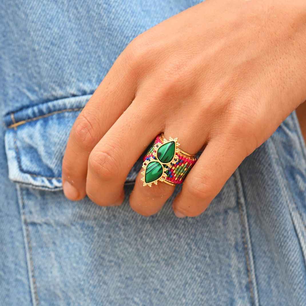 Close-up of a hand wearing a colorful ring with green gemstones on a denim background