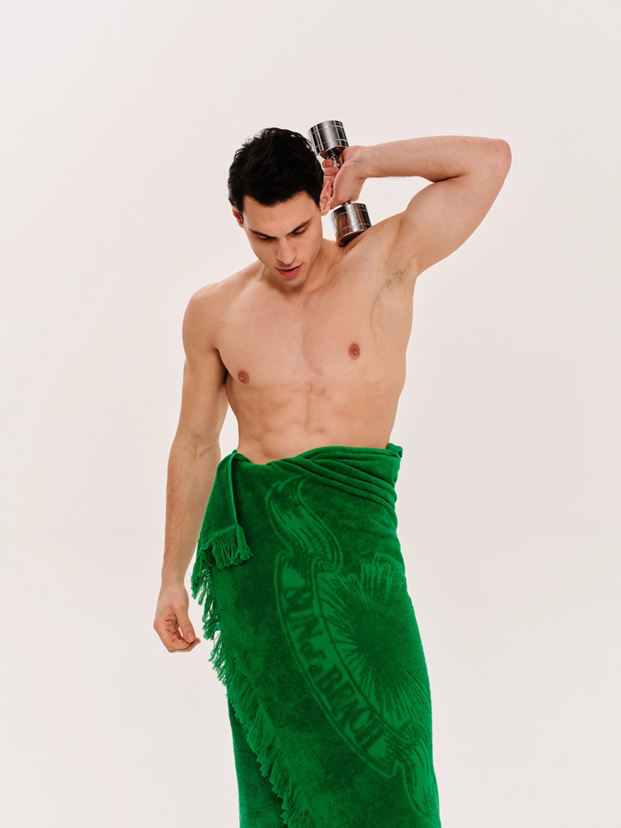 Man wearing a green sarong lifting a dumbbell on a white background