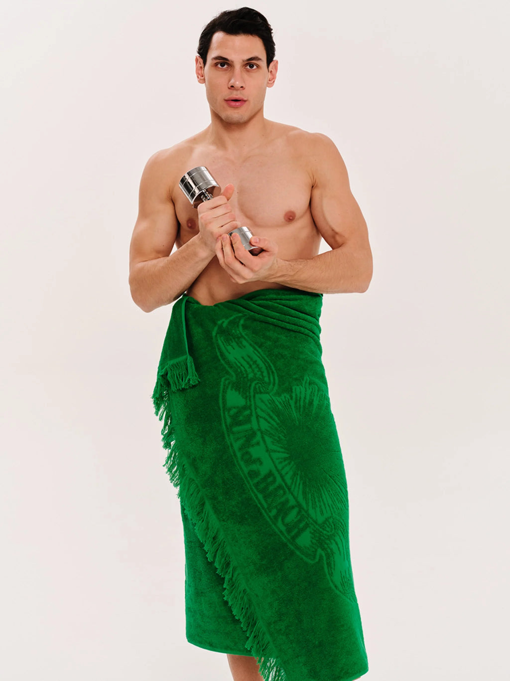 Man wearing a green sarong holding two silver bottles against a white background
