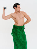 Man wearing a green towel around his waist, flexing his arm on a white background