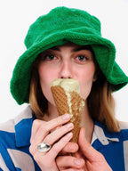 Person wearing a green hat and blue and white striped shirt, eating an ice cream cone.