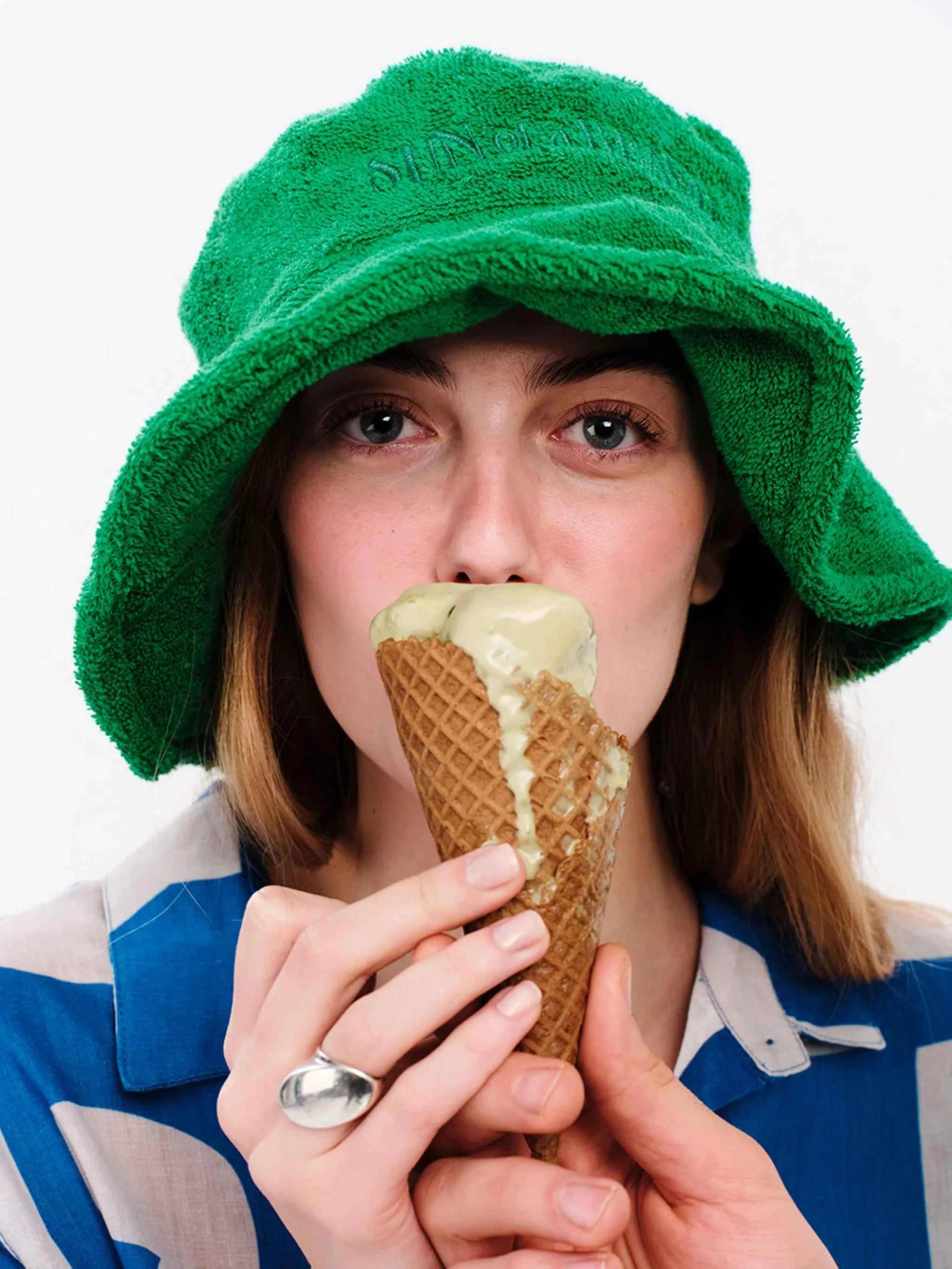 Person wearing a green hat and blue and white striped shirt, eating an ice cream cone.