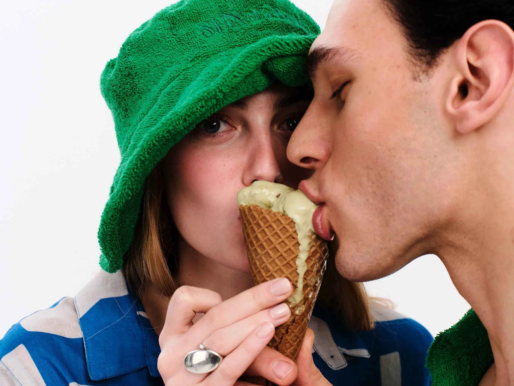 Two people sharing an ice cream cone with a green towel on their head.