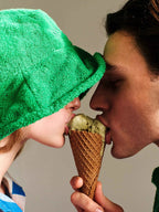 Two people sharing an ice cream cone with a green towel on one person's head.