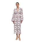 A woman modeling a long-sleeved midi dress with a white base and a large mauve-purple chain-link pattern, paired with white strappy high-heeled sandals against a plain white background.