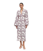 A woman modeling a long-sleeved midi dress with a white base and a large mauve-purple chain-link pattern, paired with white strappy high-heeled sandals against a plain white background.