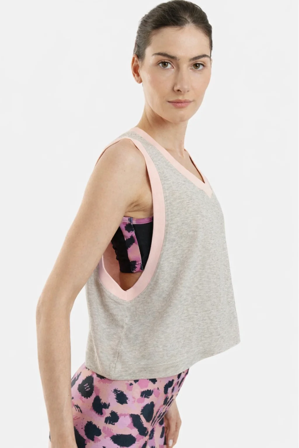 Woman wearing a gray tank top with pink trim and pink leggings with black patterns on a white background
