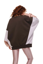 A model shown from behind wearing a colorblock sweatshirt with a dark brown back panel and light gray sleeves and side panels, paired with metallic pink leggings, on a solid white background.