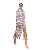 A model wearing a long-sleeved, high-slit midi dress with a white base and a dusty rose chain pattern, paired with white strappy heels, set against a plain white background.