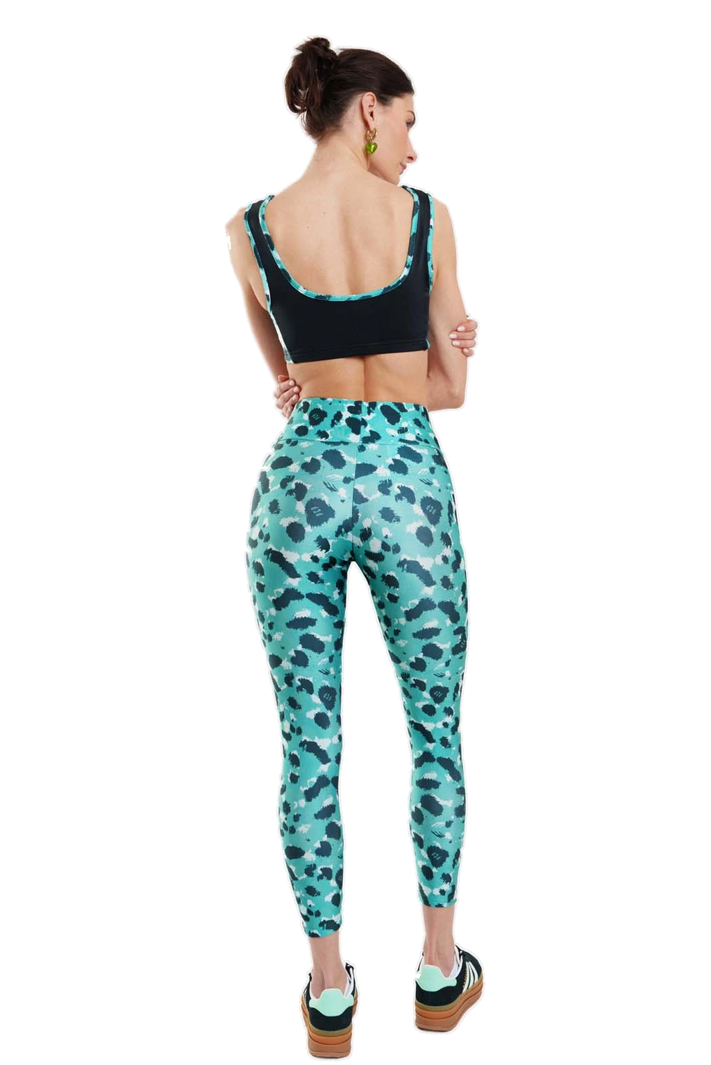 A woman is shown from the back wearing a black sports bra and high-waisted leggings with a teal and black animal print pattern, set against a plain white background.