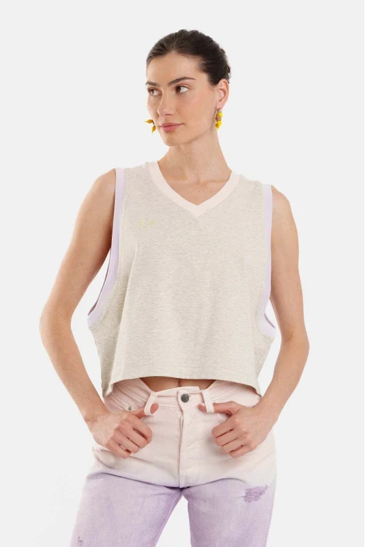 Woman wearing a sleeveless beige top and light purple jeans on a white background