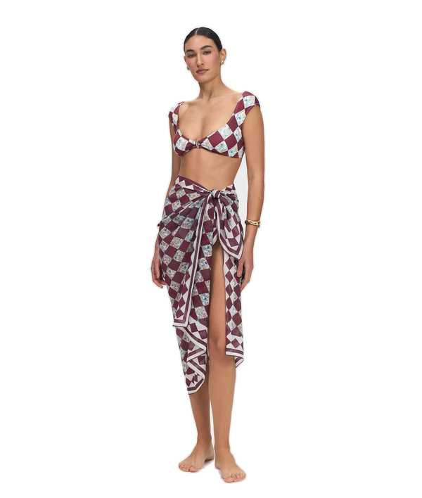 A woman modeling a matching two-piece swimwear set consisting of a halter crop top and a high-slit wrap sarong, both featuring a burgundy, white, and gray geometric diamond pattern, shot against a solid white background.