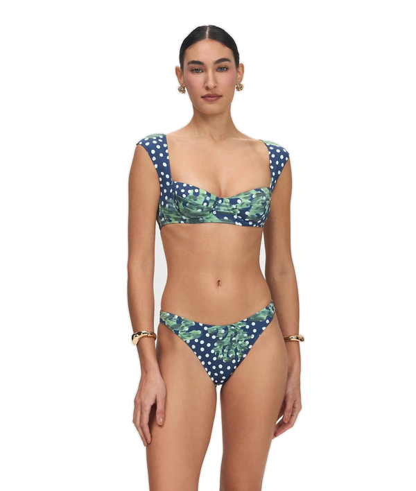 A model wearing a two-piece bikini with a green tropical leaf print and white polka dots on a solid white background.