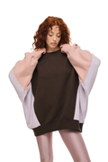 A model with curly red hair wearing a dark brown crewneck sweatshirt with oversized light pink sleeves, set against a solid white background.