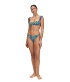 A woman modeling a two-piece bikini with a green tropical floral print on a navy blue background with white polka dots, set against a plain white studio background.