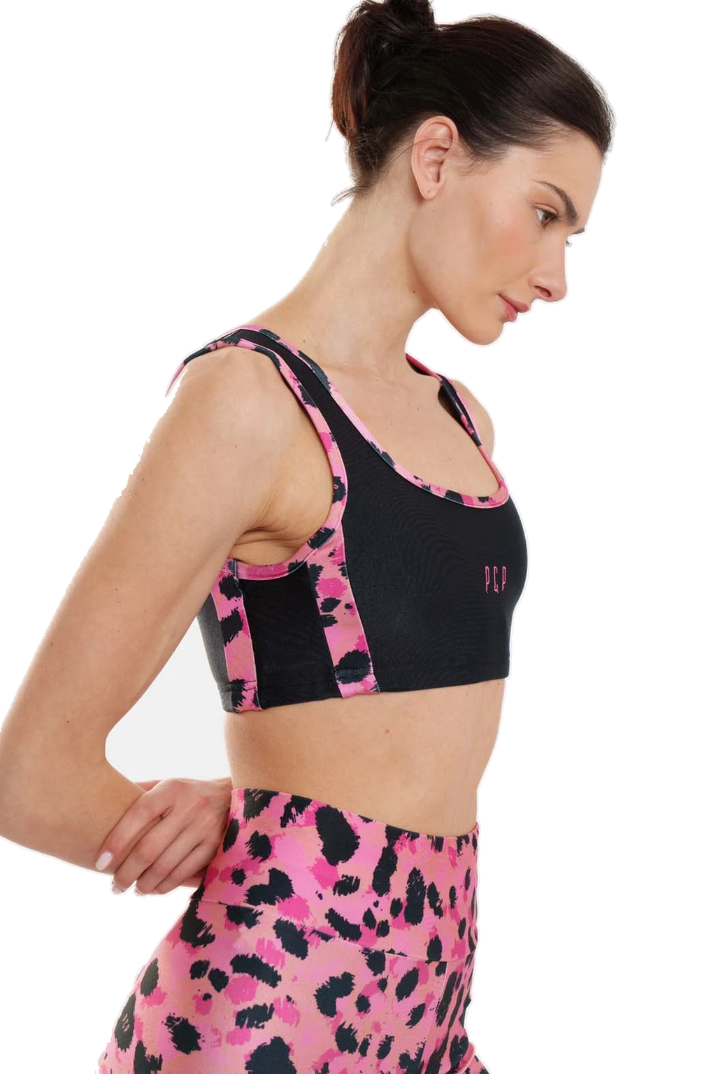 A woman wearing a black and pink leopard-print sports bra and matching high-waisted leggings, shown from a side profile against a white background.