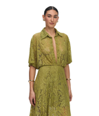 A woman modeling a short-sleeved olive green lace shirt dress with a deep V-neckline and a matching lace skirt, set against a plain white background.