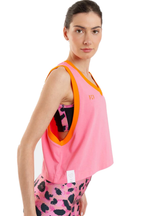 A woman modeling a pink sleeveless athletic tank top with bright orange trim, paired with pink leopard-print leggings, against a plain white background.