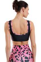 A woman shown from the back wearing a black sports bra with pink and black patterned trim and a matching pink high-waisted leggings with a black animal print, against a plain white background.