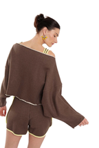 A woman modeling a brown knit two-piece set featuring an off-the-shoulder long-sleeve top and matching shorts with light yellow trim, set against a plain white background.